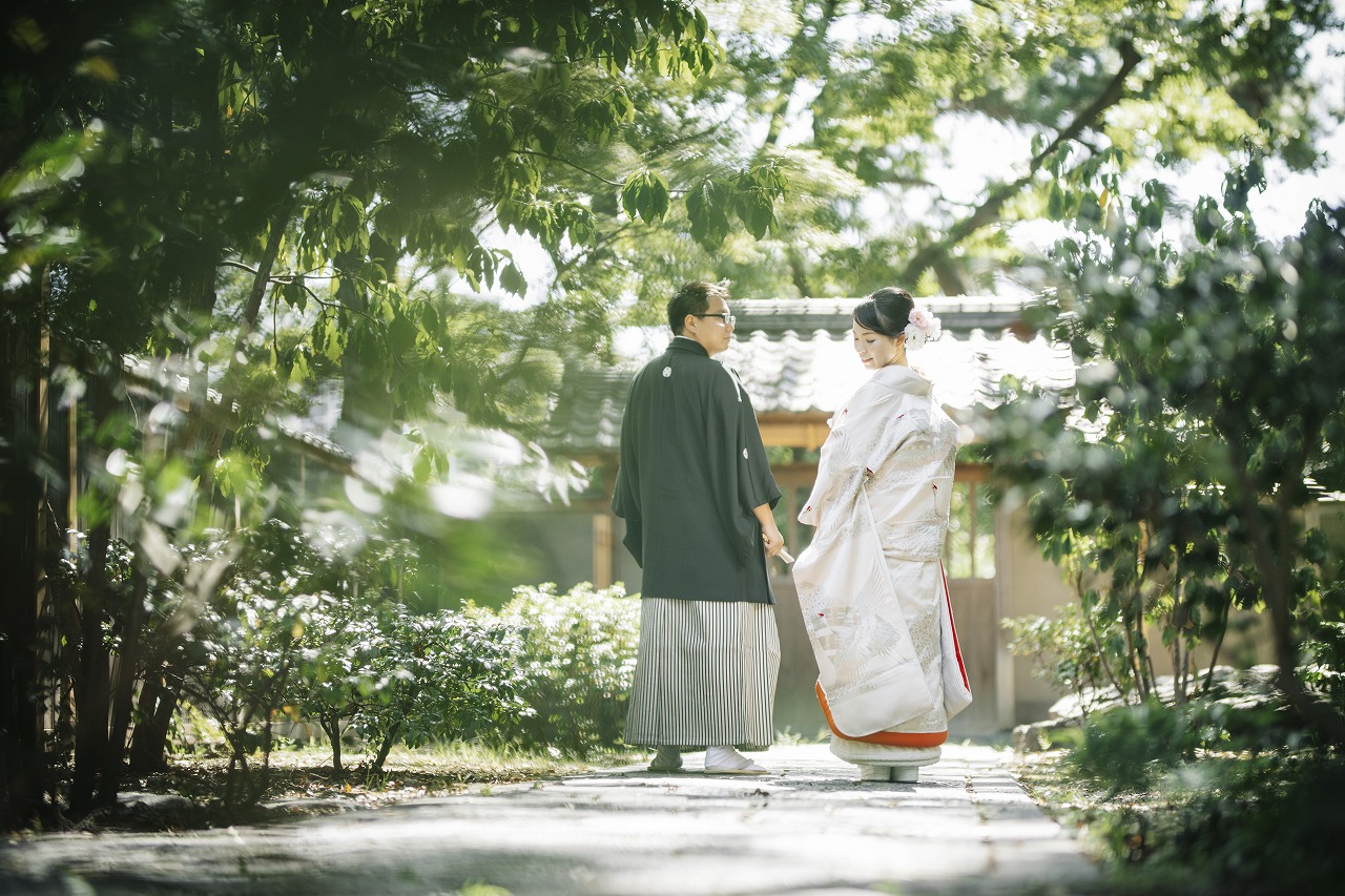 木漏れ日の落ちる小径を歩く白無垢の花嫁と紋付袴の新郎。緑に包まれた庭で撮るフォトウェディング