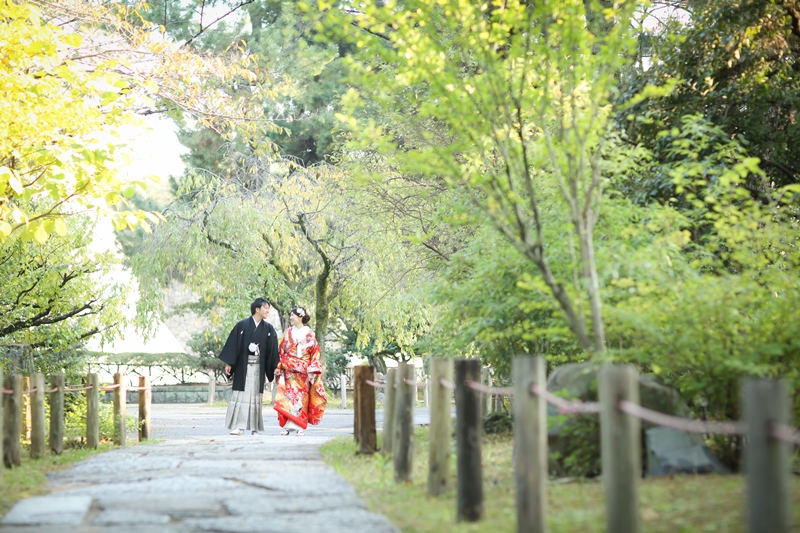 木々に囲まれた石畳の道を歩く色打掛の花嫁と紋付袴の新郎。二之丸庭園の静かなロケーションフォト