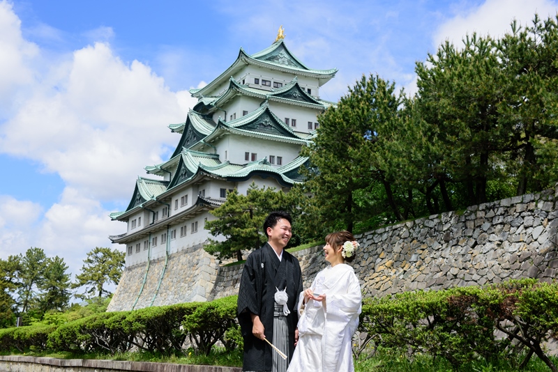 青空にそびえる天守と石垣を背にした白無垢の花嫁と紋付袴の新郎。名古屋城で撮るフォトウェディング