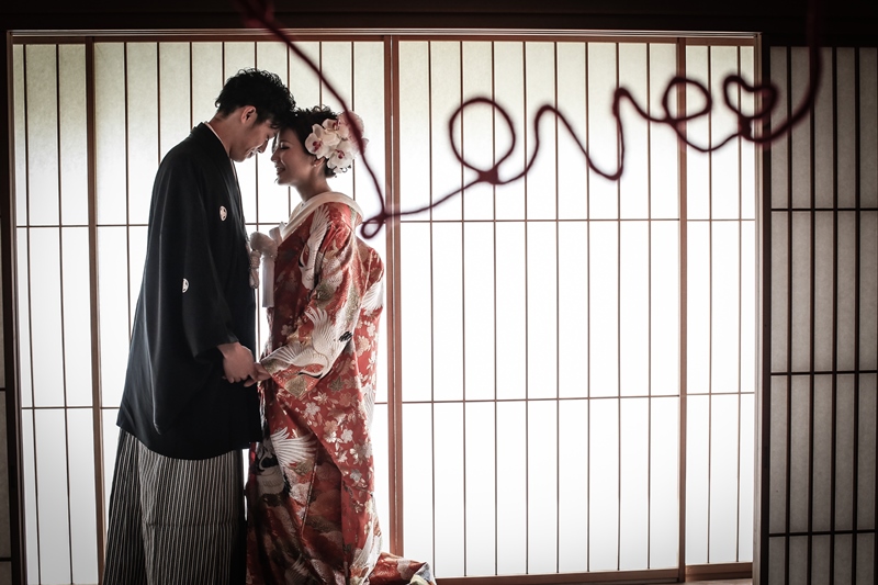障子の前で赤い紐のLOVEの文字を飾って寄り添う色打掛の花嫁と黒紋付袴の新郎。アイテムを使った結婚写真