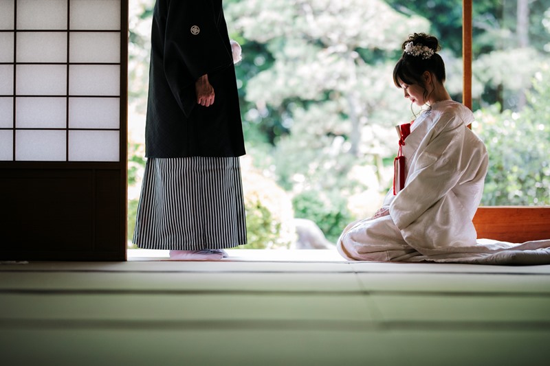 障子を開けた座敷から庭を望み、縁側で向かい合う白無垢の花嫁と黒紋付袴の新郎。静かな和装フォトウェディング