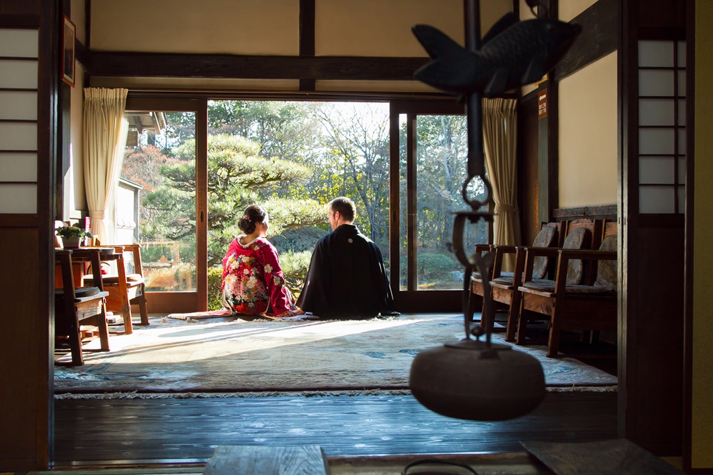 洋間の大きな窓から庭を望んで座る色打掛の花嫁と黒紋付袴の新郎。和洋の混ざる空間で撮る結婚写真
