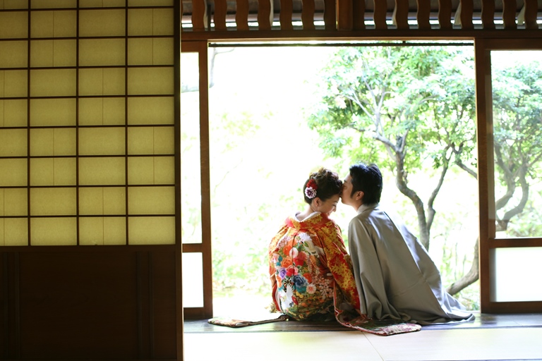 茶室の障子を開け放ち庭を眺めて座る色打掛の花嫁と紋付袴の新郎。和室で撮る落ち着いた結婚写真