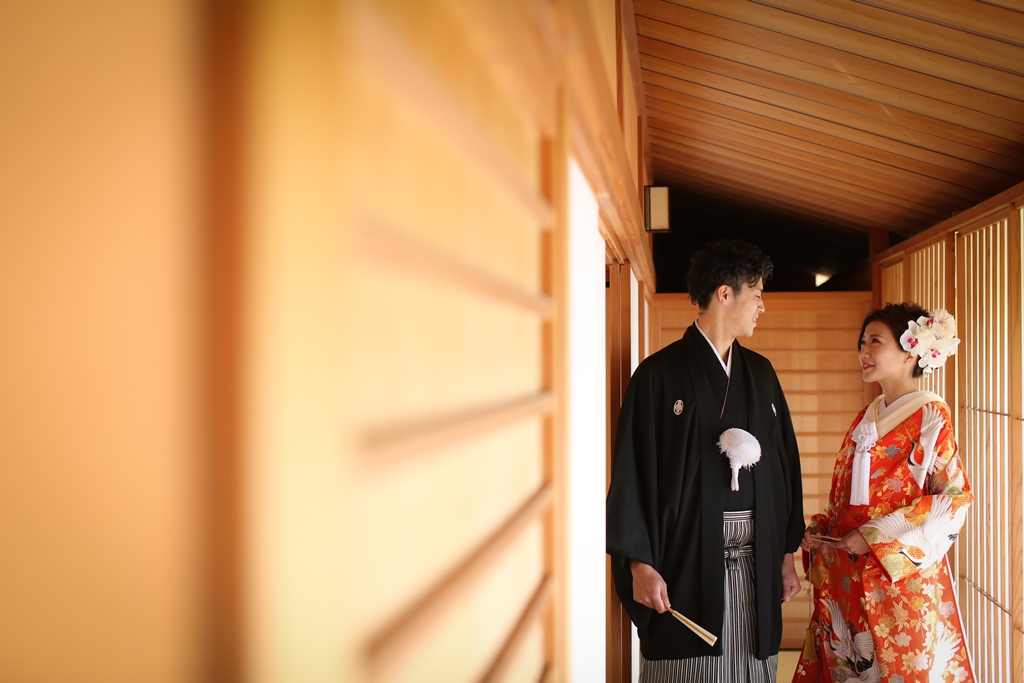 木の廊下の奥に立つ色打掛の花嫁と黒紋付袴の新郎。香流亭の建築を生かした和装ロケーションフォト