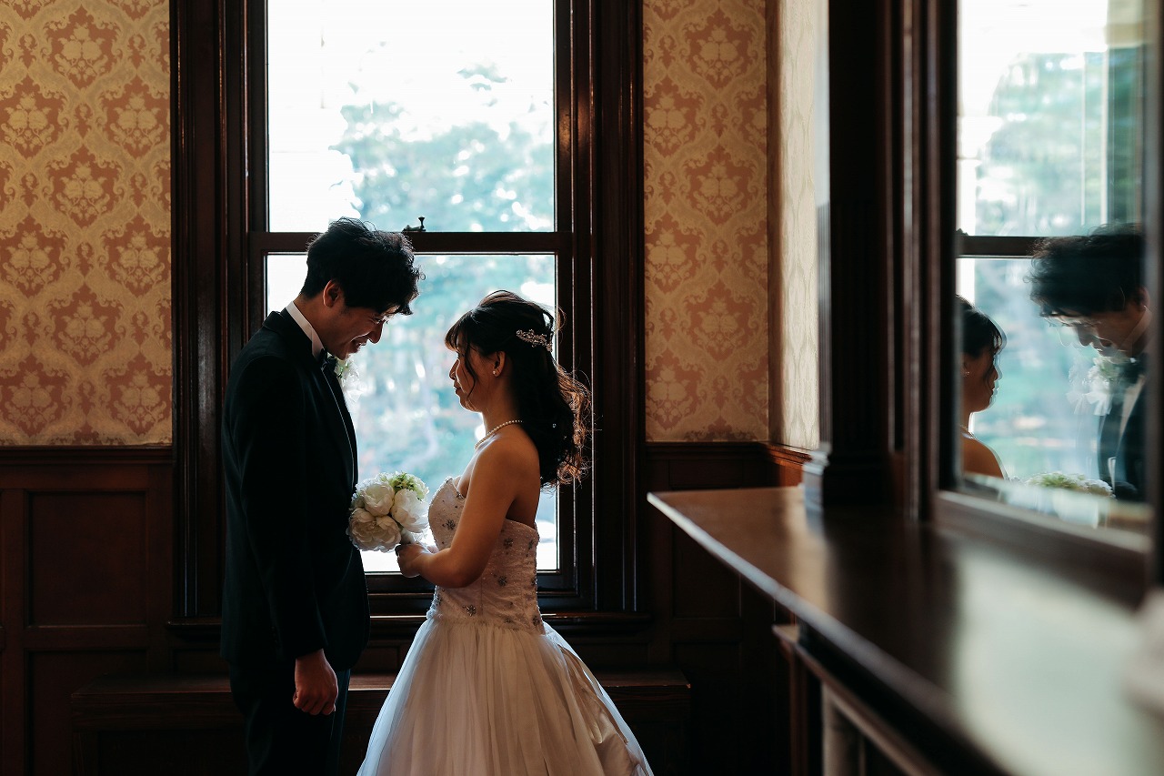 六華苑の洋館の窓辺で向かい合う、ウェディングドレスの花嫁とタキシードの新郎。クラシカルな室内で撮るフォトウェディング