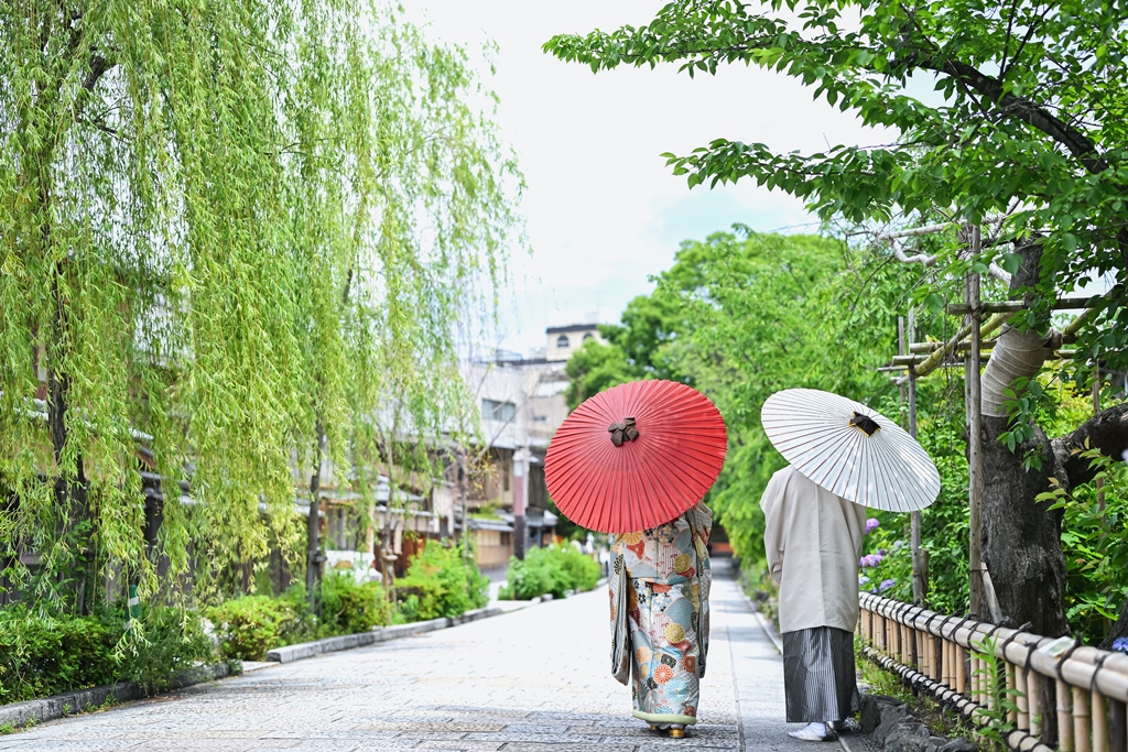 祇園の町を和傘を持って和装で歩くふたりの後ろ姿