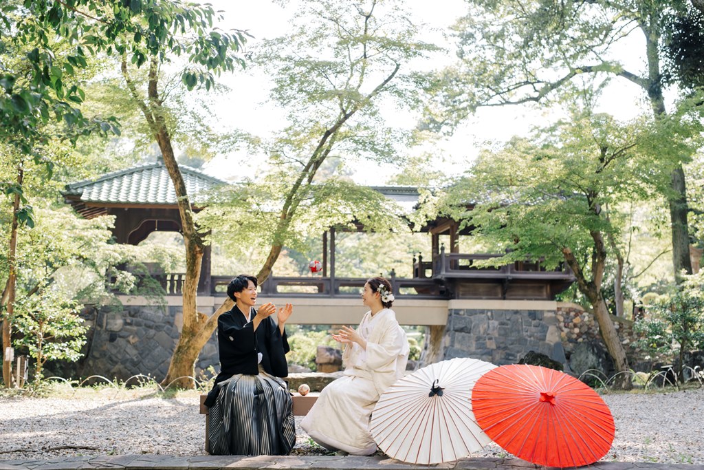 庭に椅子と和傘を置いてひと休みする白無垢の花嫁と紋付袴の新郎。和装前撮りの合間に生まれる自然な表情