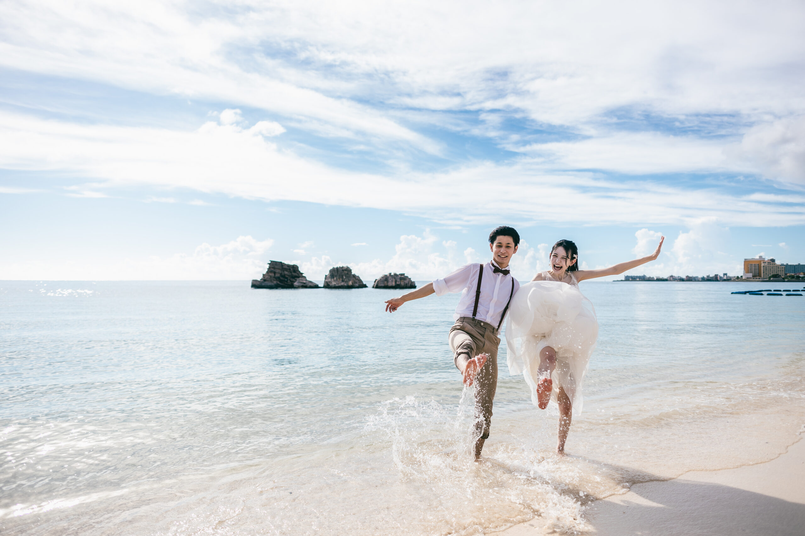 透きとおる波打ち際を手をつないで駆ける花嫁と新郎。沖縄の海で叶えるビーチフォトウェディング