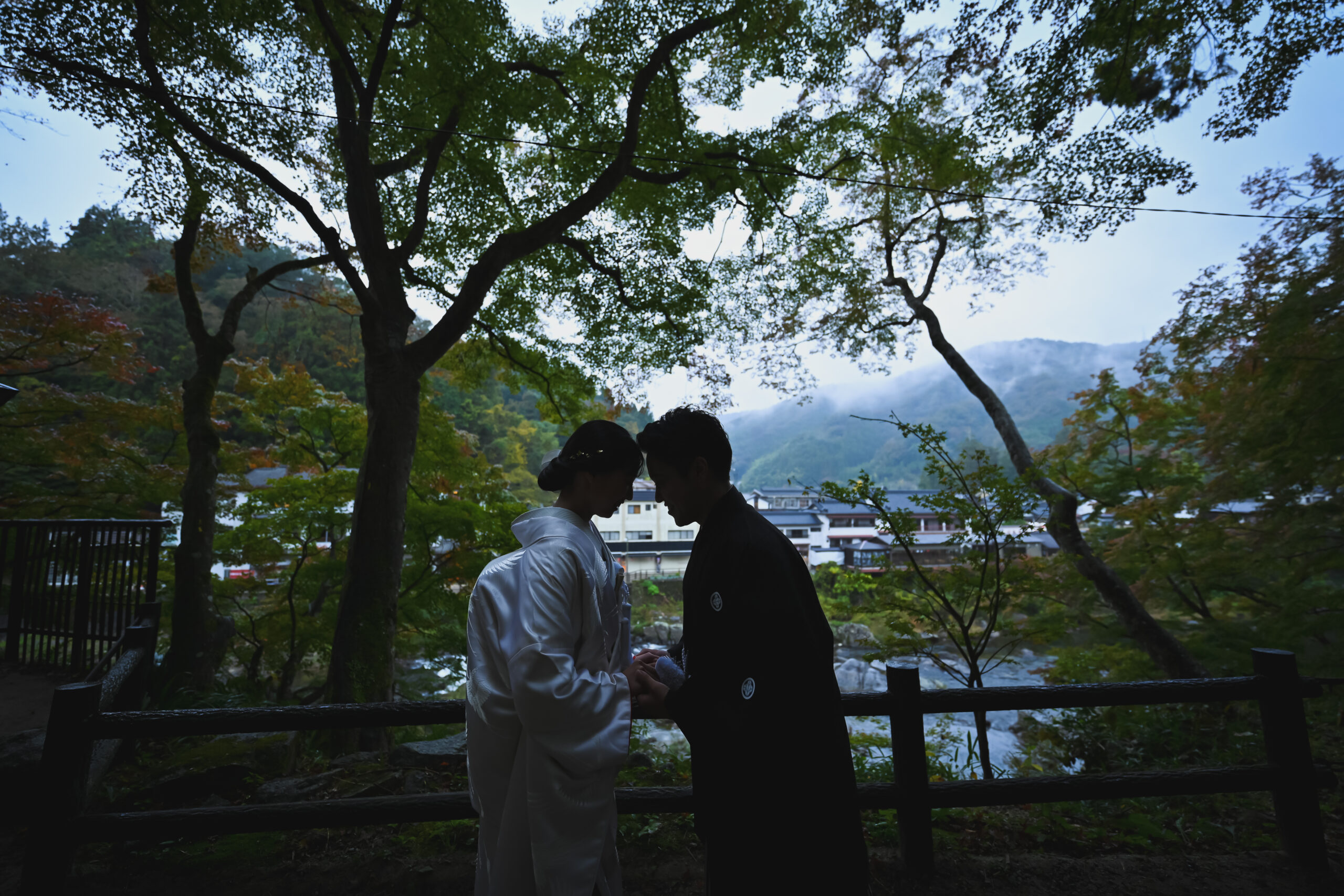 香嵐渓の川辺で朝の光を背に見つめ合う新郎新婦のシルエット。早朝だから撮れるロケーションフォト
