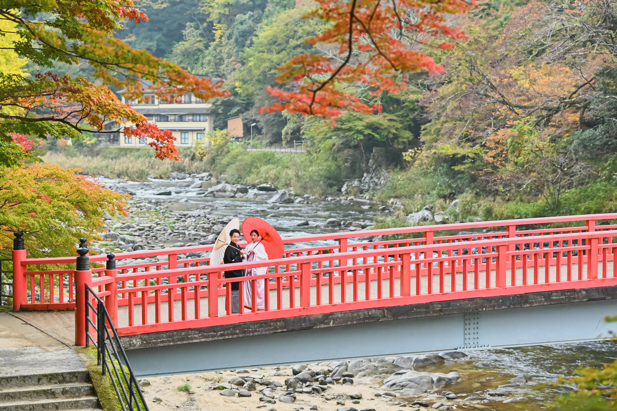 紅葉に囲まれた待月橋の上に立つ和傘の新郎新婦。橋を丸ごと入れたロケーションフォト