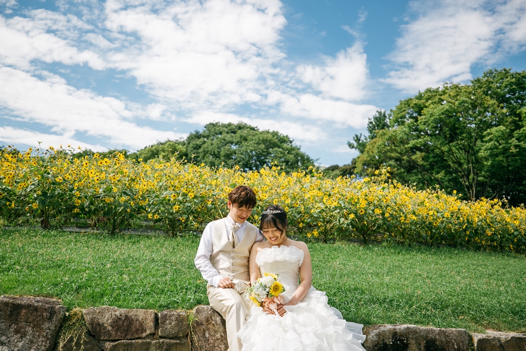 名城公園の青空と芝生を背景にドレスをなびかせて歩くカップル