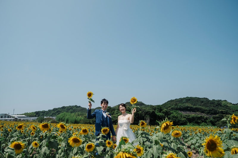 ひまわりを手に持ちほほ笑む白ドレスの花嫁