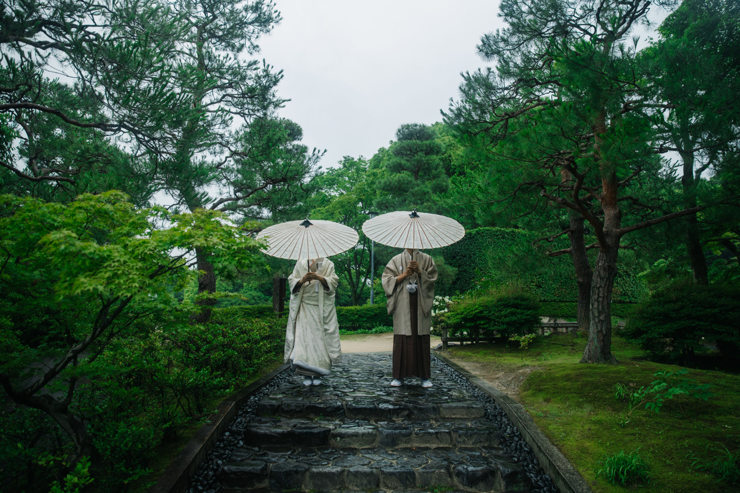 雨の日に透明な傘をさして見つめ合う洋装カップルの幻想的なロケーション撮影