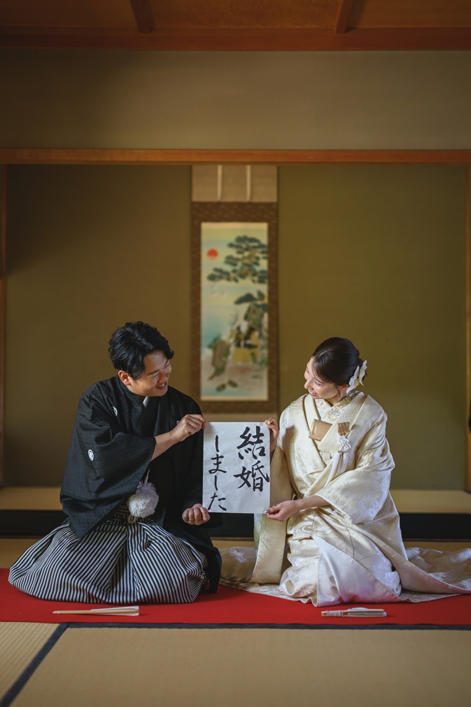 和装の花嫁と新郎が習字の書かれた半紙を手に持って撮影したオリジナリティある写真