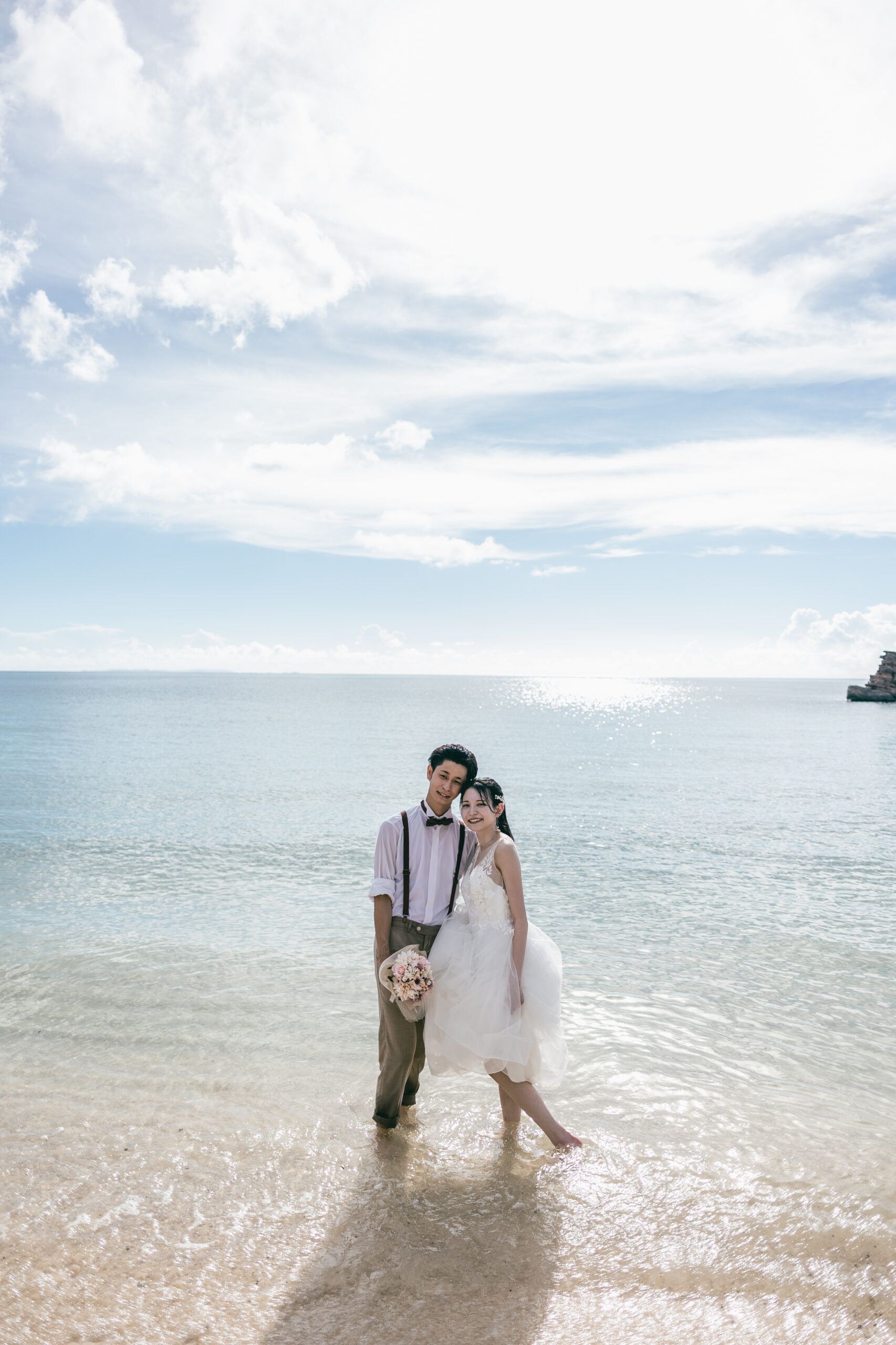 青空と海を背景に撮影する新郎新婦