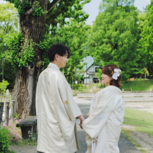 大木の下で手を取り合って見つめ合う白い羽織袴の新郎と白い色打掛の花嫁。岡崎公園で撮る和装前撮り