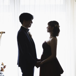 白いカーテンの窓を背に、手を取り合って見つめ合う新郎新婦のシルエット。逆光を生かした名古屋のスタジオ前撮り