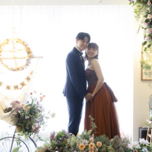 花の装飾とMR＆MRSのガーランドを背に、逆光の中で寄り添う新郎新婦。カラードレスで撮る名古屋のスタジオフォト