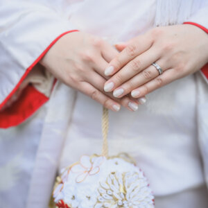 白い花の髪飾りを添えた白無垢の胸元に重ねた花嫁の手と結婚指輪のアップ。和装前撮りの手元カット