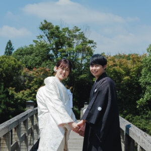 木の橋の上で手をつなぐ白い色打掛の花嫁と黒紋付袴の新郎を引きでとらえた一枚。白鳥庭園で撮る和装ロケーションフォト
