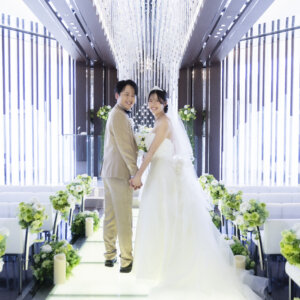 シャンデリアの光が降り注ぐバージンロードで、両手をつないで向き合う新郎新婦。ラグナヴェール名古屋で残す写真だけの結婚式