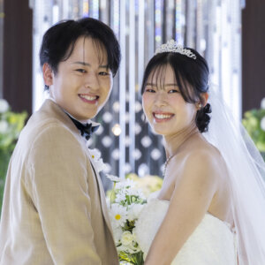 祭壇の装花を背に、頬を寄せて満面の笑みを見せる蝶ネクタイの新郎とティアラの花嫁。名古屋のチャペルで撮るウェディングフォト