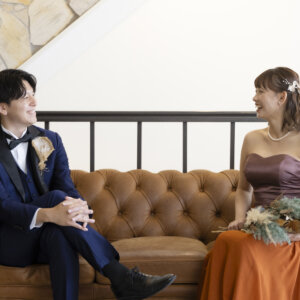 レザーソファに座って向かい合い、笑い合う新郎新婦。ドライフラワーのブーケとカラードレスで撮る名古屋のナチュラルなスタジオ前撮り