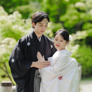新緑の下で花嫁の手を取る黒紋付袴の新郎と、目を伏せる白無垢の花嫁。白鳥庭園で撮る和装前撮り