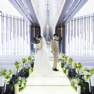 光あふれるバージンロードの奥で、少し離れて立つ新郎とブーケを持つ花嫁。ラグナヴェール名古屋のクリスタルのチャペルで叶えるフォトウェディング