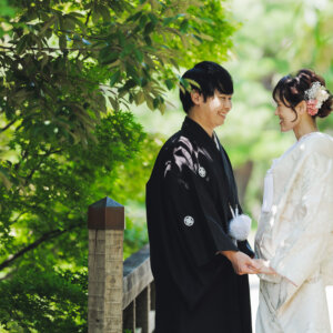 木漏れ日の下で手を取り合って見つめ合う黒紋付袴の新郎と白い色打掛の花嫁。白鳥庭園で撮る和装前撮り