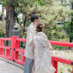 朱い橋の欄干のそばで寄り添う白い羽織袴の新郎と白い色打掛の花嫁の後ろ姿。岡崎公園で撮る和装前撮り