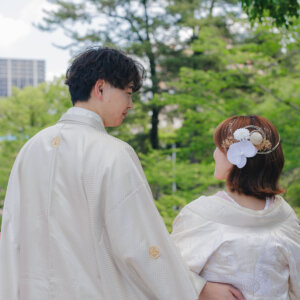朱い欄干の前で見つめ合う白い羽織袴の新郎と花の髪飾りの白い色打掛の花嫁の後ろ姿。岡崎公園で撮る和装前撮り