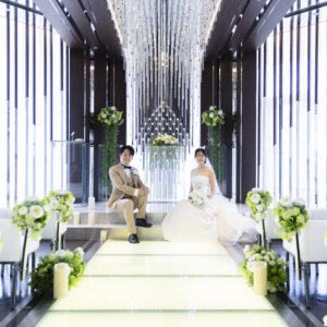クリスタルのシャンデリアが連なるチャペルの祭壇の階段に腰を下ろす新郎新婦を、バージンロードの先から撮ったフォトウェディング
