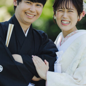 腕を組んで満面の笑みを見せる黒紋付袴の新郎と白い色打掛の花嫁のアップ。和装前撮りの笑顔のポートレート