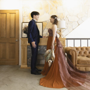 レザーソファと暖炉のある洋館風のスタジオで向かい合う新郎新婦。テラコッタのカラードレスのロングトレーンが床に広がる名古屋のスタジオフォト