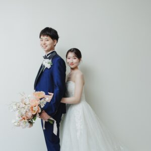 新郎の後ろから顔を出してほほえむ花嫁と、ブーケを持つタキシードの新郎。名古屋のスタジオで撮る洋装の結婚写真