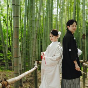 竹林の柵のそばで見つめ合う白無垢の花嫁と黒紋付袴の新郎。白鳥庭園の竹林で撮る和装前撮りのロケーションフォト
