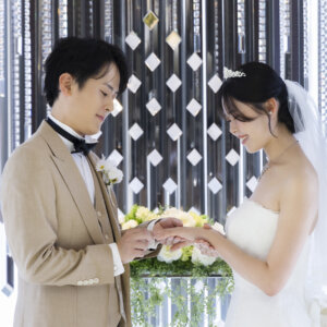 ラグナヴェール名古屋のチャペルの祭壇前で、ベージュのタキシードの新郎が花嫁の指に結婚指輪をはめる指輪交換のシーン。写真だけの結婚式ならではの一枚