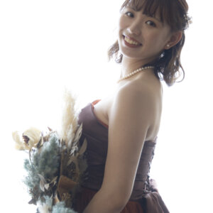 白い背景で振り返って微笑む、ビスチェのカラードレスの花嫁。ドライフラワーのブーケを後ろ手に持った逆光のスタジオフォト