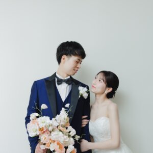 腕を組んで見つめ合うネイビーのタキシードの新郎とウェディングドレスの花嫁。白い背景で撮った名古屋のスタジオ前撮り