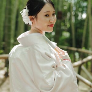 竹林で白い花の髪飾りを付けて振り返る白無垢の花嫁の後ろ姿。竹林で撮る和装前撮りのブライダルポートレート