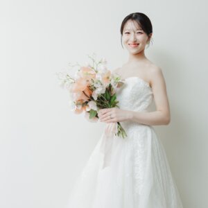 白い背景の前でブーケを手に笑顔を見せるビスチェのウェディングドレスの花嫁。名古屋のスタジオで撮った洋装前撮り