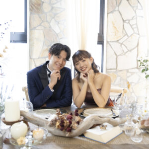 ドライフラワーとキャンドルを飾ったテーブルで、頬杖をついて笑う新郎新婦。カフェのような空間で撮る名古屋のスタジオ前撮り
