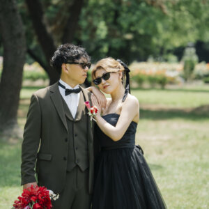 サングラスをかけて寄り添うオリーブのスーツの新郎と黒いドレスの花嫁。庄内緑地で撮る洋装前撮りの遊び心のあるカット