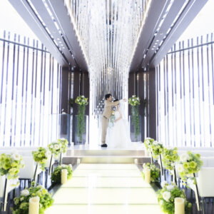 祭壇で向き合い、誓いのように手を取る新郎新婦をバージンロードの中央から写した全景ショット。名古屋で叶える写真だけの結婚式