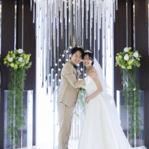 グリーンの装花とクリスタルに囲まれた祭壇前で、抱き合ってカメラに笑顔を向ける新郎新婦。ラグナヴェール名古屋の結婚写真