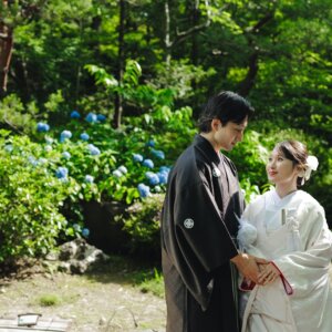 紫陽花の咲く庭で手を取り合う黒紋付袴の新郎と白無垢の花嫁。初夏の白鳥庭園で撮る和装ロケーションフォト