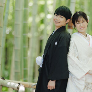 竹林で背中合わせに立って笑う黒紋付袴の新郎と白無垢の花嫁。白鳥庭園の竹林で撮る和装前撮りの背中合わせポーズ