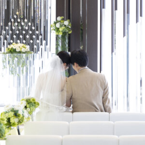 白いソファ席に並んで座り、祭壇を見つめる新郎新婦の後ろ姿。ラグナヴェール名古屋のチャペルで残す穏やかなフォトウェディング