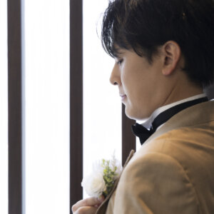 胸元にブートニアを付けたベージュのタキシードの新郎が、目を伏せて静かにたたずむ横顔。チャペルで撮る新郎ソロの結婚写真